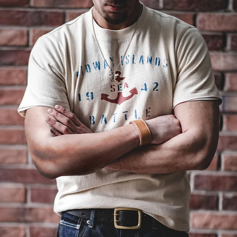 Person wearing a beige t-shirt with text and graphics against a brick wall